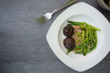 Fried asparagus and shiitake with oyster sauce in white dish on concrete table.