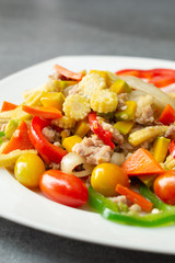 Stir fried vegetables with sweet pepper,tomato,pumpkin,corn and chicken in white dish on concrete table.