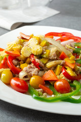 Stir fried vegetables with sweet pepper,tomato,pumpkin,corn and chicken in white dish on concrete table.