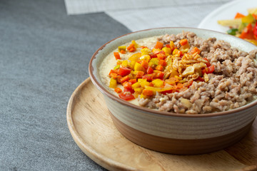 Beaten steamed egg with sweet pepper,carrot and chopped chicken in brown bowl on concrete table.