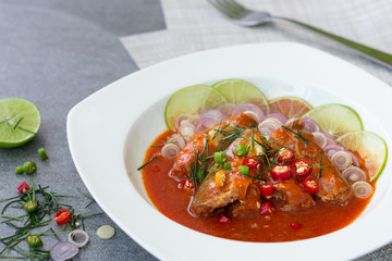 Spicy sardine salad with tomato sauce in white dish on concrete table.