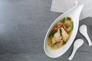 Sour and spicy soup with chicken drumstick in white bowl on concrete table.