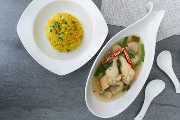 Sour and spicy soup with chicken drumstick and in white bowl and fried rice with turmeric in white dish on concrete table.