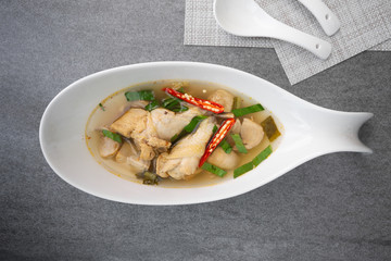 Sour and spicy soup with chicken drumstick in white bowl on concrete table.