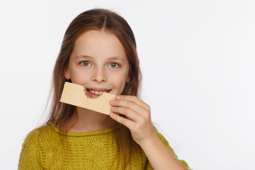 Portrait of a beautiful 8 year old girl in a sweater and with a wafer in her hand. White background