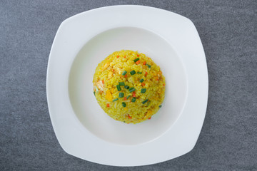 Fried rice with turmeric,carrot,egg and coriander or Yellow fried rice in white dish on concrete table.