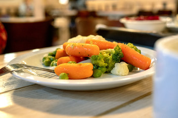 Vegetarian or lenten food. Carrots, cauliflower and green peas on a plate in the kitchen on the table.