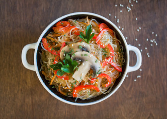 glass noodles with vegetables and mushrooms in a plate on a brown background. Top view, close-up