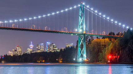 Vancouver, British Columbia. Canada View at night of the Lions Gate Bridge with lights trail, glitters and clouds on a full moon sky.