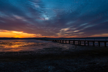 A long jetty on large tidal lake at sunset.