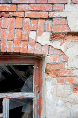 Fragment of a window with a wooden frame on a brick wall of an old house. Glazing destroyed, plaster fell off.
