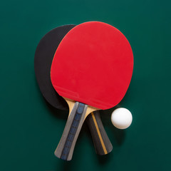Two ping-pong rackets and a ball on a green table. C