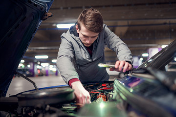 Man with phone in hand mending broken car with open hood.