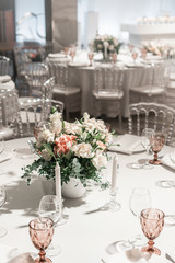 Flower arrangement in the center of the table. Interior of restaurant for wedding dinner, ready for guests. Round Banquet table served. Catering concept.