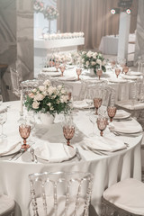Wine glasses on round Banquet table served. Interior of restaurant for wedding dinner, ready for guests. Decorated with floral arrangement. Dishes, wine glasses and napkins. Catering concept.