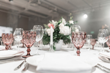 Wine glasses on round Banquet table served. Interior of restaurant for wedding dinner, ready for guests. Decorated with floral arrangement. Dishes, wine glasses and napkins. Catering concept.