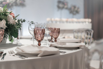 Glasses of wine on round Banquet table served. Interior of restaurant for wedding dinner, ready for guests. Decorated with floral arrangement. Dishes, wine glasses and napkins. Catering concept.