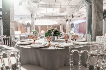 Round Banquet table served. Interior of restaurant for wedding dinner, ready for guests. Decorated with floral arrangement. Dishes, wine glasses and napkins. Catering concept.