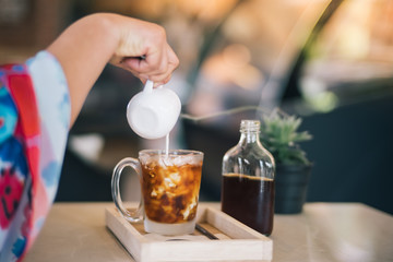 Hand of woman hold a cup and pouring a coffee in to cup with ice cream on wooden table. Cafe affogato.