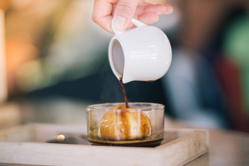 Hand of woman hold a cup and pouring a coffee in to cup with ice cream on wooden table. Cafe affogato.