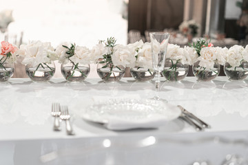 Small flower arrangements in ball glass vases. The table of the newlyweds. Interior of restaurant for wedding dinner, ready for guests. Catering concept.