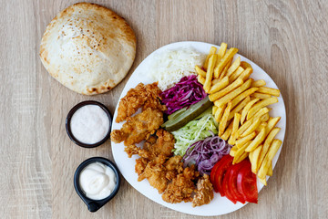 Chicken wings on the plate with bread, sauce, french fries, tomatoes, onion, pickles and cabbage salad on a wooden background.