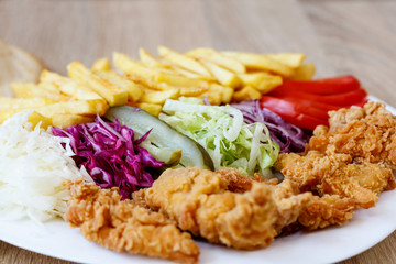 Chicken wings on the plate with french fries, tomatoes, onion, pickles and cabbage salad on a...