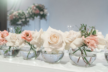 Small flower arrangements in ball glass vases. The table of the newlyweds. Interior of restaurant for wedding dinner, ready for guests. Catering concept.