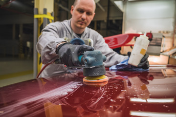 Employee in the shop painting the car body polishes painted body parts