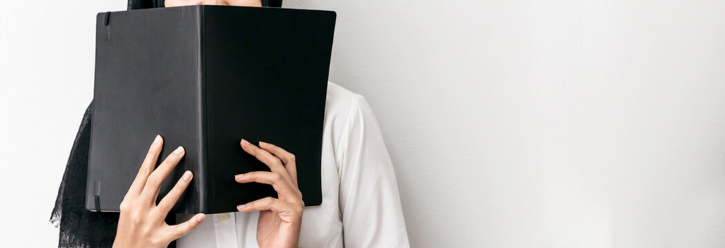 Muslim Woman Wearing Hijab, White Shirt And Holding A Black Cover Book In Front Of Her With Copy Space.