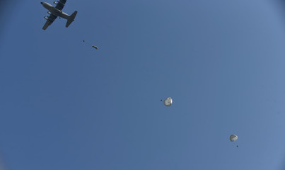 Airplane is dropping three parachutes with blue sky in background