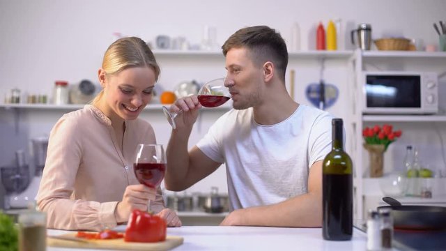 Young couple drinking wine in kitchen, chatting and relaxing together, romance