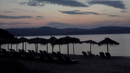 Sunset silhouettes of straw umbrellas and sunbeds on the beach