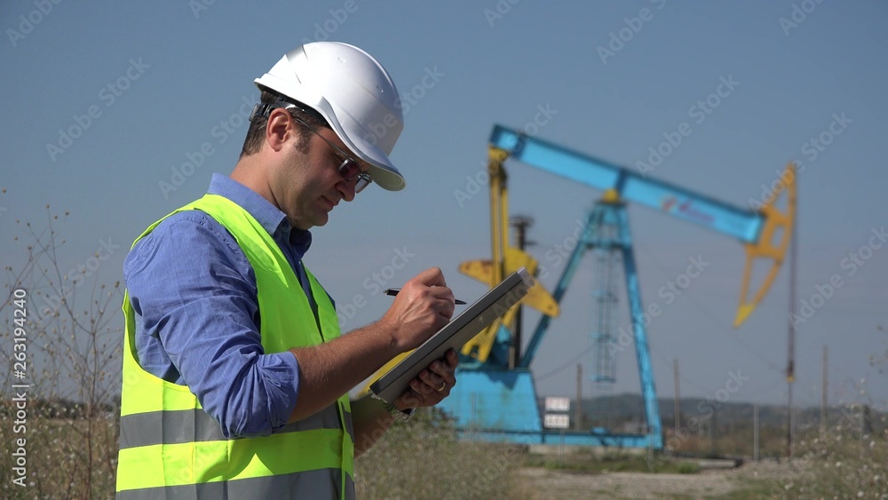 Wall mural young engineer writing down information close oil pump