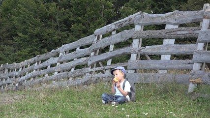 Naklejka na ściany i meble Lovely child with a backpack eating apple, resting on green grass near wooden fence