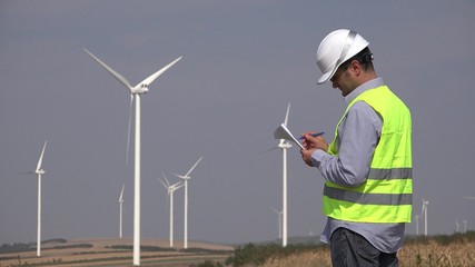 Engineer near windmills turbines writing down the technical parameters