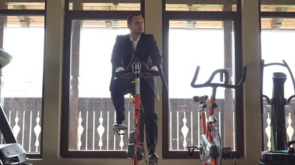 Man with suit training at static bicycle at gym, break at work