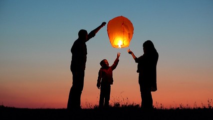 Parents, child and baby silhouette rising lightning sky lantern, conceptual release hope, free dreams of happy family
