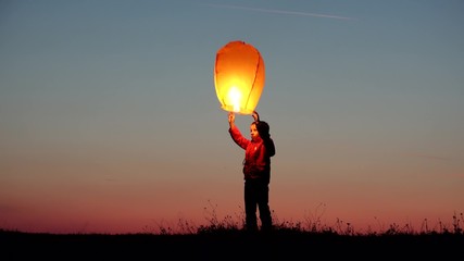 Little child holds lightning chinese sky lantern and release it on red sunset sky, happy kid jumping for free dreams, conceptual - Powered by Adobe