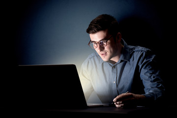 Young handsome businessman working late at night in the office with a dark background