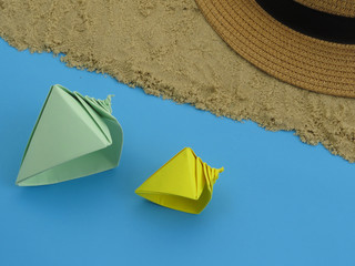 Origami seashells and straw hat on sand on a blue background