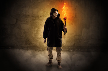 Ugly wayfarer with burning torch in his hand in front of a crumbly wall concept
