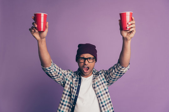 Close up photo portrait of cheerful glad mad drunk carefree in eyeglasses guy holding rising holding in hands palms big bright plastic glasses with beverage isolated violet background