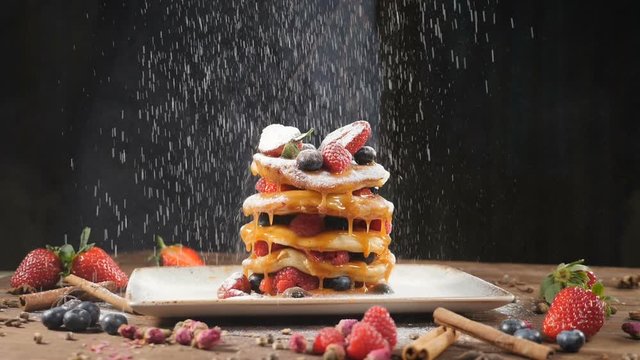 Sugar powder being poured over pancakes beautifully served with berries and caramel syrup. Food art. Dessert and breakfast concept. Closeup shot. pastry pour sugar. Slow motion. hd