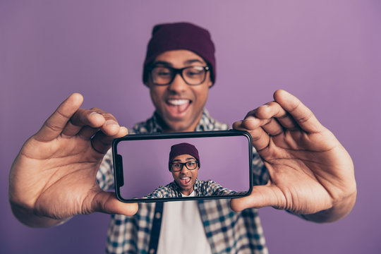 Closeup photo portrait of cheerful excited laughing screaming fooling millenial influencer holding smart phone in hands making taking selfie on instagram isolated violet background