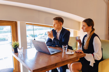 A stylish couple drinks morning coffee at the cafe and works with a laptop, young businessmen and freelancers