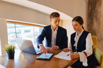 young businessmen boy and girl work with a laptop, a tablet and notes in the cafe