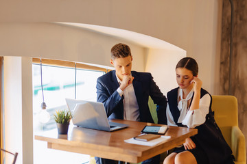 young businessmen boy and girl work with a laptop, a tablet and notes in the cafe
