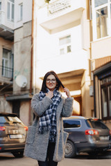 Fototapeta premium Attractive positive young girl wearing glasses in a coat on the background of buildings on cars