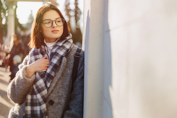 Attractive young girl wearing glasses in a coat walking on a sunny day